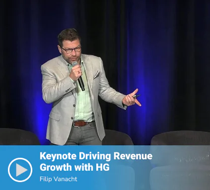 Video thumbnail of a keynote titled "Driving Revenue Growth with HG" featuring speaker Filip Vanacht presenting on stage in a light gray blazer, holding a microphone and gesturing, against a dark blue-lit backdrop.