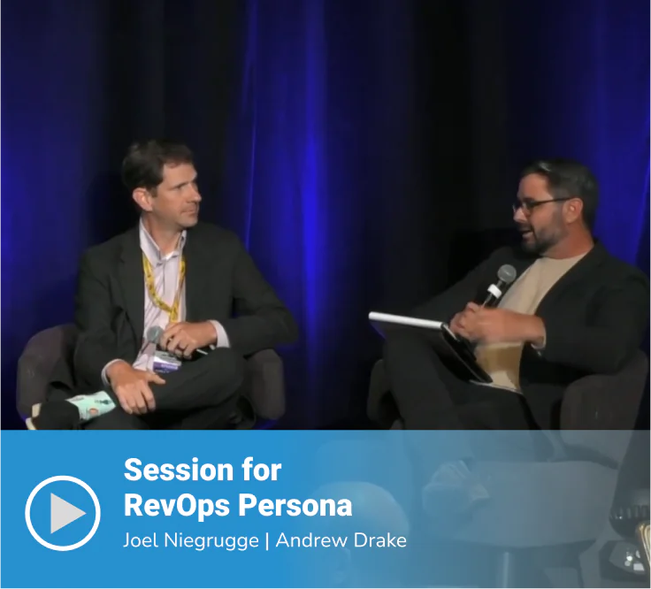 Video thumbnail of a "Session for RevOps Persona" featuring speakers Joel Niegrugge and Andrew Drake seated on stage in conversation, with Andrew holding a microphone and tablet, against a dark blue-lit backdrop.