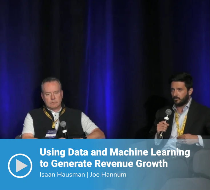 Video thumbnail of a panel session titled "Using Data and Machine Learning to Generate Revenue Growth" featuring speakers Isaan Hausman and Joe Hannum seated on stage, with Joe speaking into a microphone, against a dark blue-lit backdrop.