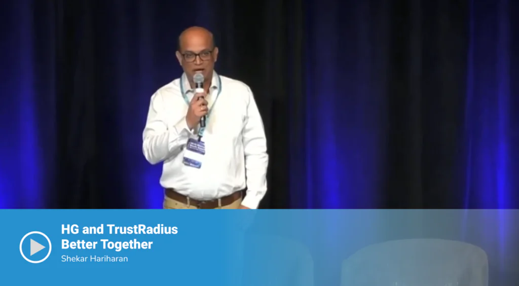 Video thumbnail of a session titled "HG and TrustRadius Better Together" featuring speaker Shekar Hariharan standing on stage holding a microphone, against a dark blue-lit curtain backdrop.