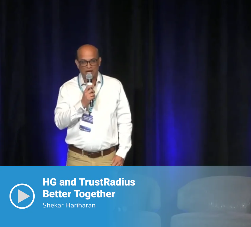 Video thumbnail of a session titled "HG and TrustRadius Better Together" featuring speaker Shekar Hariharan standing on stage holding a microphone in a white shirt, against a dark blue-lit curtain backdrop.